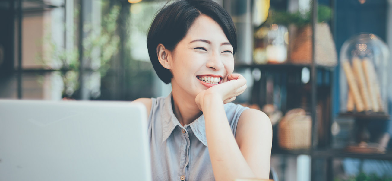 A woman in front of her lap top looking over and smiling.